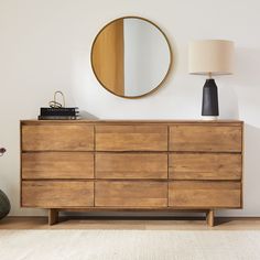 a wooden dresser with a round mirror above it and a lamp on the sideboard