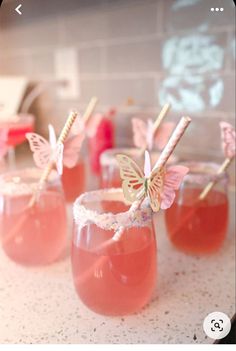 three glasses filled with pink liquid and butterfly straws on top of each glass, sitting on a counter