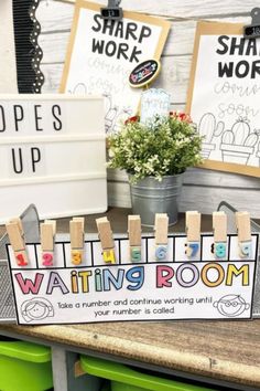 a sign that says waiting room with clothes pegs on it and some potted plants