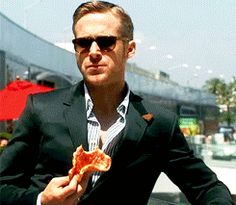 a man in a suit and sunglasses holding a slice of pizza