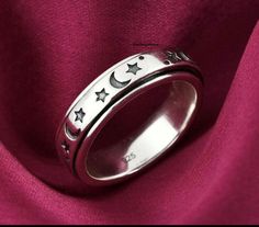 a silver ring with stars and crescents on the inside, sitting on a pink fabric