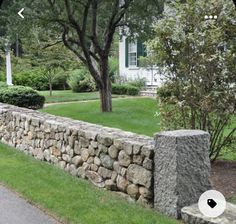 a stone wall in front of a house with trees and grass on the side walk