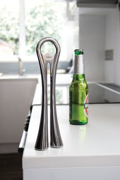 a bottle opener sitting on top of a white counter next to a green beer in a glass bottle