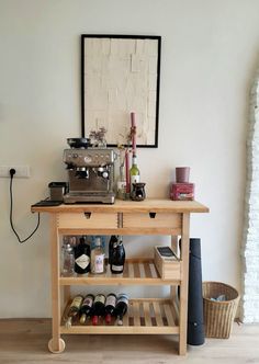 a wooden table topped with bottles of wine next to a wall mounted clock and pictures