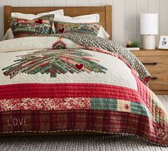 a bed with a red and green quilt on it's headboard next to a night stand