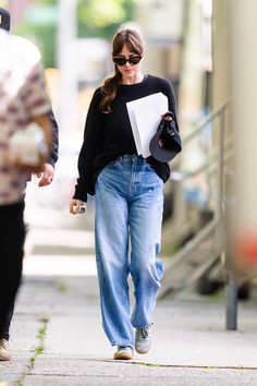 a woman in black sweater and jeans walking down the street