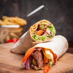 a burrito cut in half sitting on top of a cutting board next to french fries