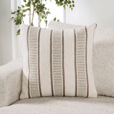 a close up of a pillow on a couch with a plant in the back ground