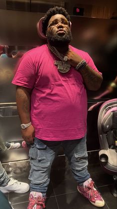 a man in a pink shirt and headphones standing next to a mirror with his hand on his hip