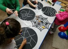 three children are sitting at a table with spider webs on it and one child is drawing