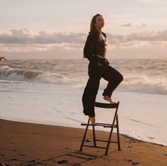 a woman standing on top of a chair in front of the ocean