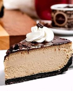 a slice of cheesecake with whipped cream and chocolate sauce on top, sitting on a white plate