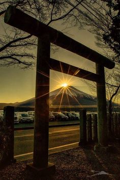 the sun is setting behind a large wooden structure on the side of the road with mountains in the background