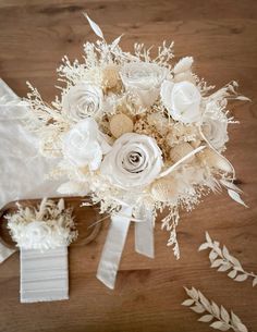 a bridal bouquet with white flowers and greenery on a wooden table next to a pair of scissors