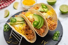 three tacos with shredded cheese, avocado and jalapenos on a plate