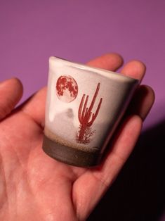 a hand holding a small cup with a desert scene on it