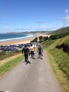 three people are walking down the road with their surfboards