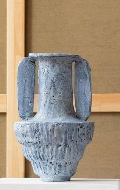 an old blue vase sitting on top of a white table next to a brown wall