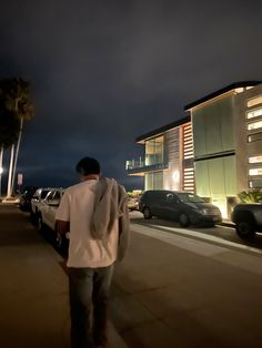 a man is walking down the street in front of some parked cars at night time