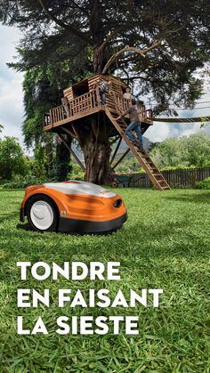 an orange and white lawn mower sitting in the grass next to a tree house