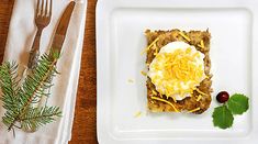 a white plate topped with food on top of a wooden table next to a fork and knife