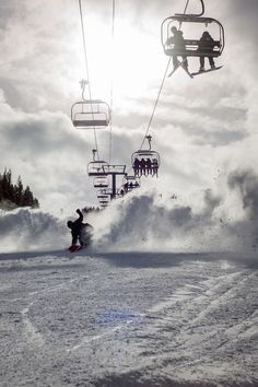 a person riding a snowboard on a snowy slope under a ski lift with people in the background