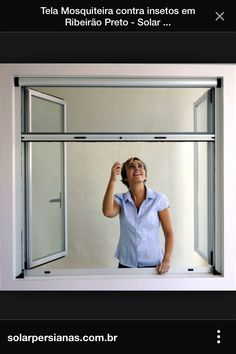 a woman standing in front of a window with her hand up to the sky and smiling