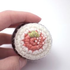 a hand is holding a crocheted object in the shape of a button with a flower on it