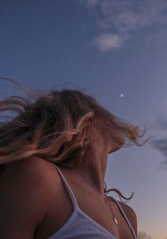 a woman with her hair blowing in the wind at sunset or dawn, looking up into the sky