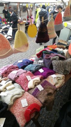 several knitted hats and sweaters are on display at an open air market stall