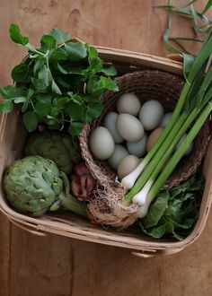 a basket filled with eggs and vegetables on top of a wooden table next to green leaves