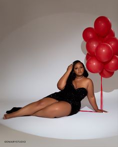 a woman sitting on the floor next to a bunch of red balloons in front of her