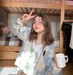 a woman sitting on the floor holding a coffee cup and peace sign in front of her face