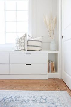 a white shelf with some pillows on top of it next to a rug and window