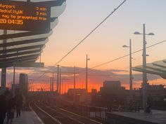 the sun is setting at an empty train station with people walking on the platform near it