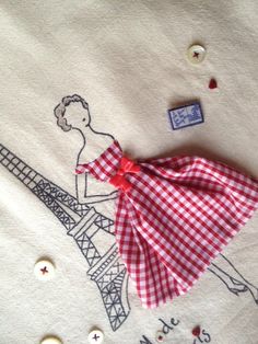 a red and white checkered dress laying on top of a piece of cloth next to a button