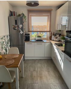 a kitchen with white cabinets and wood flooring next to a dining table in front of a window