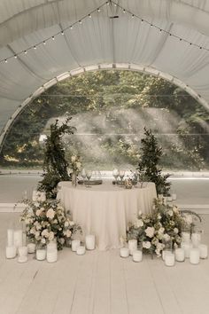 a table is set up with candles and flowers for an outdoor wedding reception in a tent