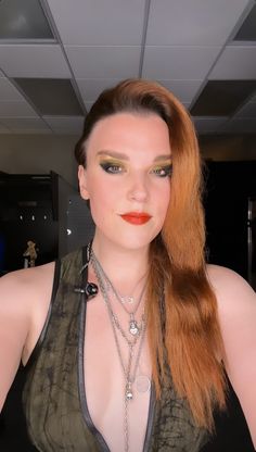 a woman with long red hair and green eyeshade wearing necklaces on her neck