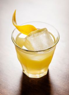 a glass filled with lemonade and ice on top of a wooden table next to a slice of lemon