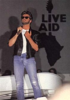 a man standing on top of a stage with a microphone in his hand and wearing sunglasses