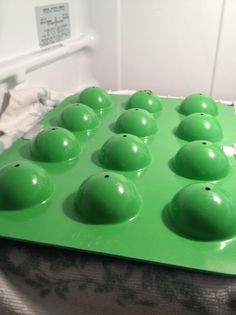 a green muffin tray filled with lots of chocolate balls on top of a bed