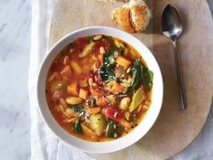 a white bowl filled with vegetable soup next to a piece of bread on top of a cutting board