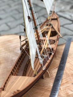 a model sailboat sitting on top of a wooden table next to a measuring tape