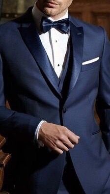 a man in a blue tuxedo standing next to a wooden table wearing a white shirt and bow tie