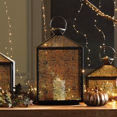 three decorative lanterns sitting on top of a wooden table next to string lights and pumpkins