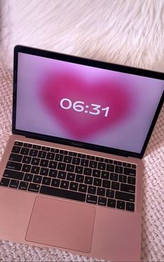 an open laptop computer sitting on top of a white bed next to a pink heart