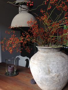 a vase with some red berries in it sitting on a table next to a candle