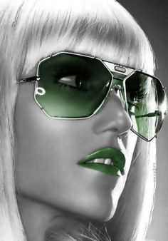 a woman wearing green sunglasses with red lips and long white hair is looking off to the side