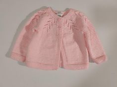 a pink knitted cardigan sweater hanging on a white wall with the tag attached to it